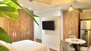 Une chambre d’hôtel moderne équipée d’un lit, d’une table à manger avec des chaises, d’un téléviseur fixé au mur et d’un réfrigérateur.