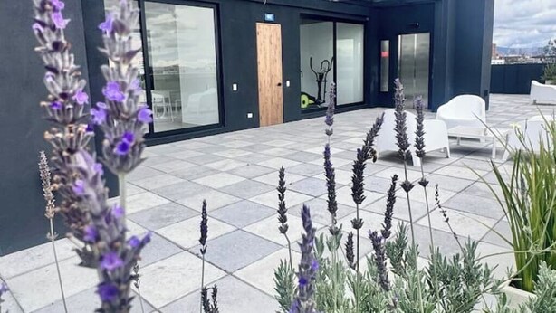 Une terrasse sur le toit au design moderne, comprenant un espace salon avec des chaises blanches et une entrée avec une porte en verre.