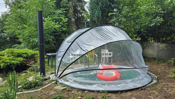 A transparent tent-like structure with a circular base, surrounded by greenery and a fence. - Vacation apartment in the village (Pürgen)