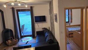 A cozy living room with a fireplace, a sofa, a TV, and a view of the outdoors. - Vacation apartment in the village (Pürgen)