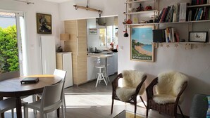 A modern kitchen with white cabinets, a dining area with a wooden table and white chairs, and a cozy seating area with wicker chairs. - In l'Herbaudière, 100 m from the sea, 5 mn from the port, ideal house for 4 people (L'Herbaudière - Noirmoutier-en-l'île)