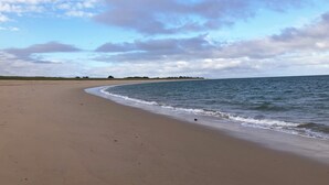 A wide sandy beach with gentle waves, a clear sky, and distant greenery. - In l'Herbaudière, 100 m from the sea, 5 mn from the port, ideal house for 4 people (L'Herbaudière - Noirmoutier-en-l'île)