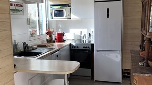 A modern kitchen with white cabinetry, a microwave, a stove, and a refrigerator. There is a small island with stools and a sink. - In l'Herbaudière, 100 m from the sea, 5 mn from the port, ideal house for 4 people (L'Herbaudière - Noirmoutier-en-l'île)
