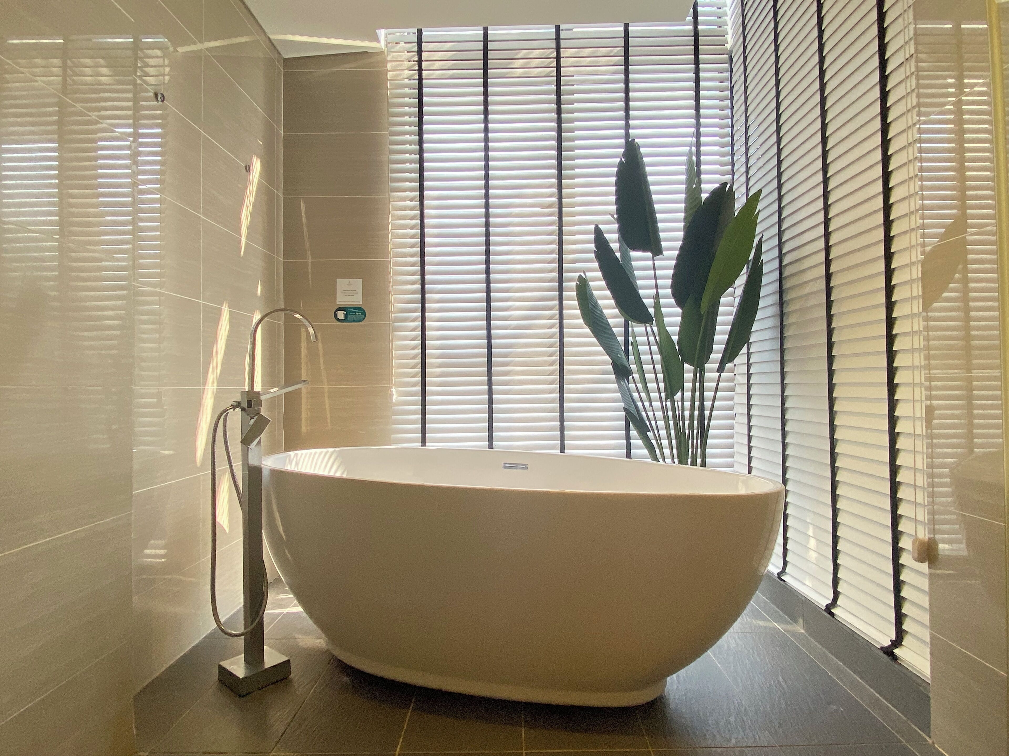 A modern bathroom with a freestanding bathtub, a towel rack, and a potted plant.