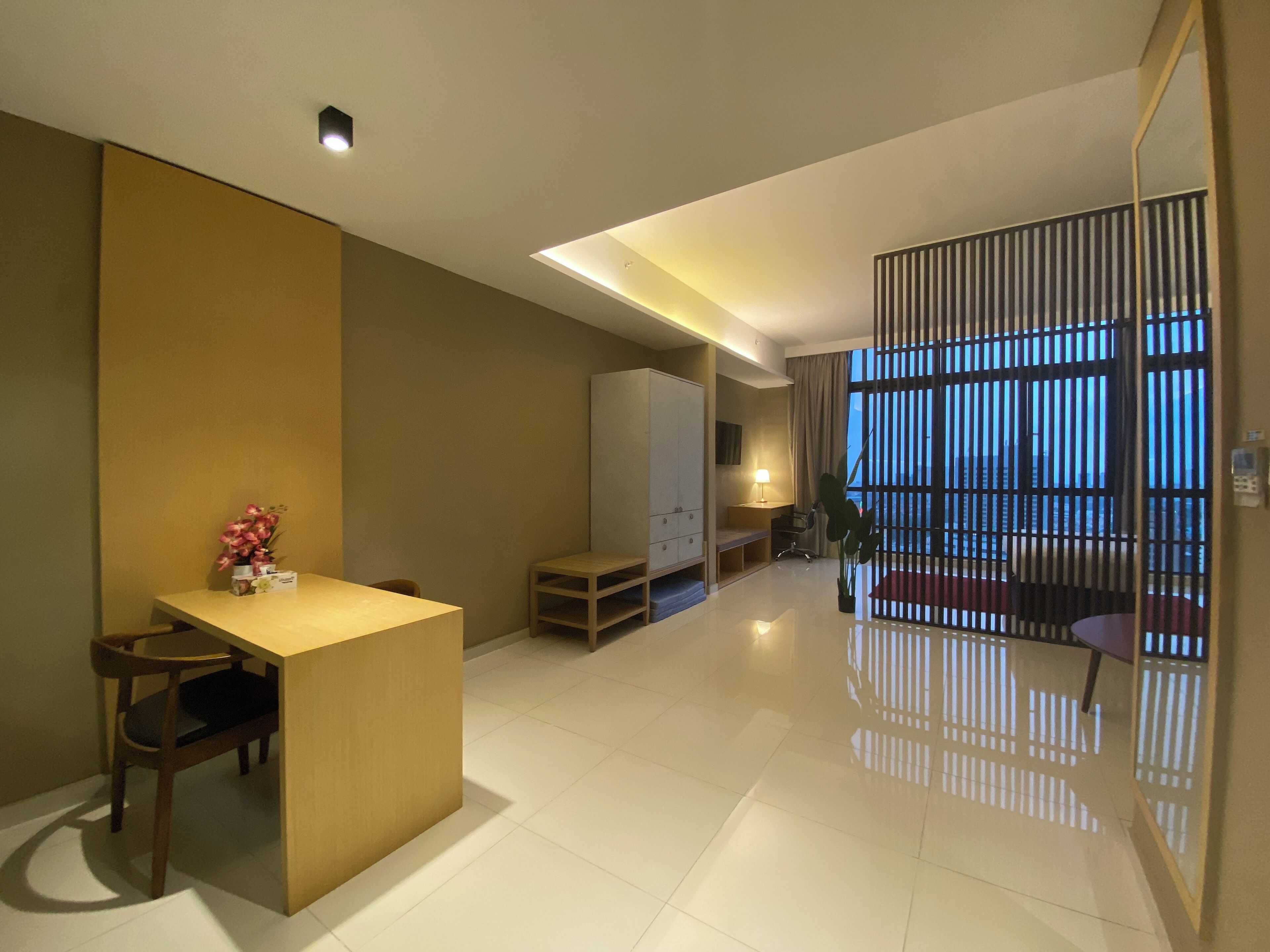 A modern hotel room with a dining area, a bed, a desk, and a large window with blinds.