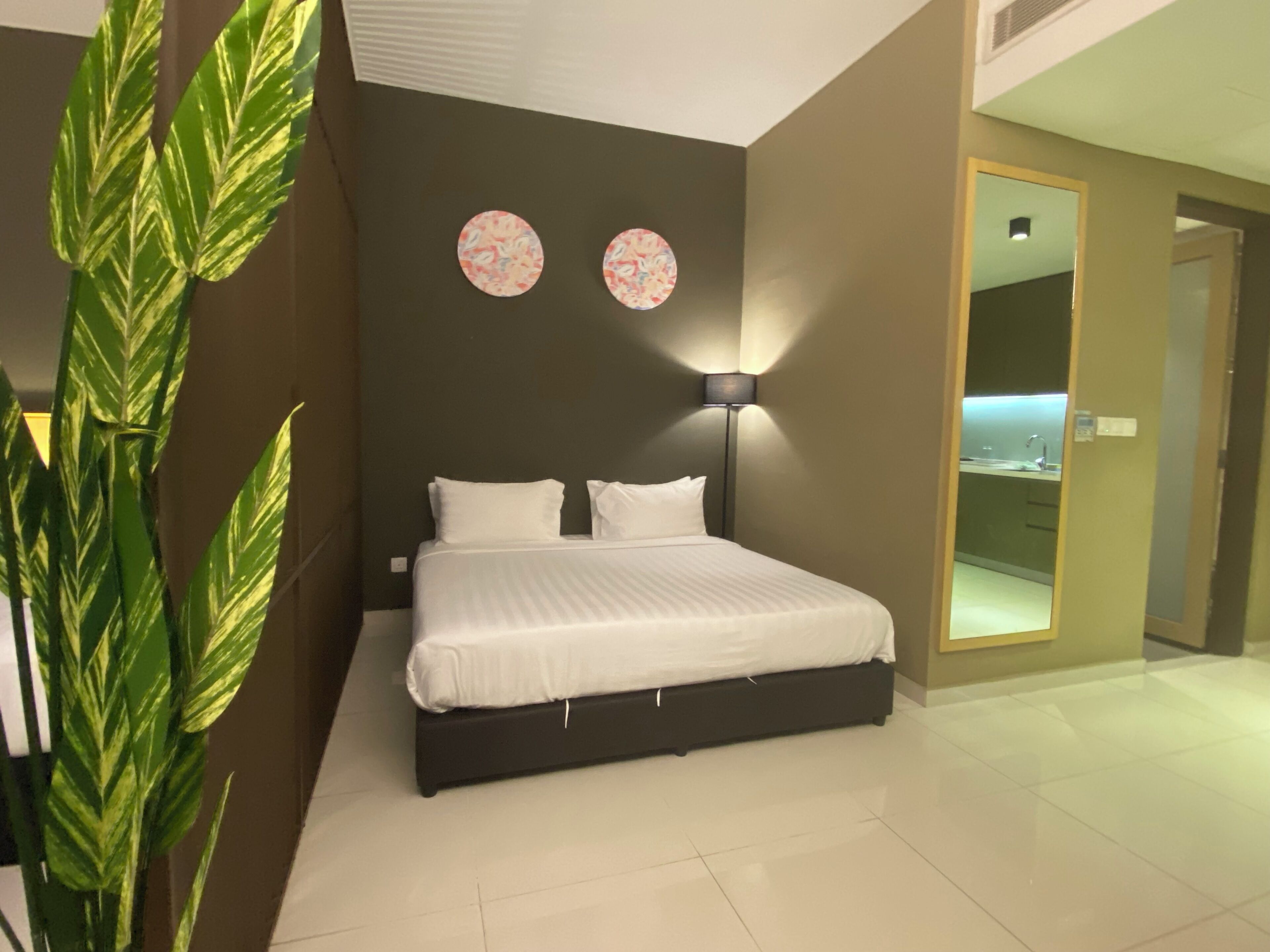 Een moderne slaapkamer met een groot bed, een nachtkastje, een wandlamp en een plant in een pot.