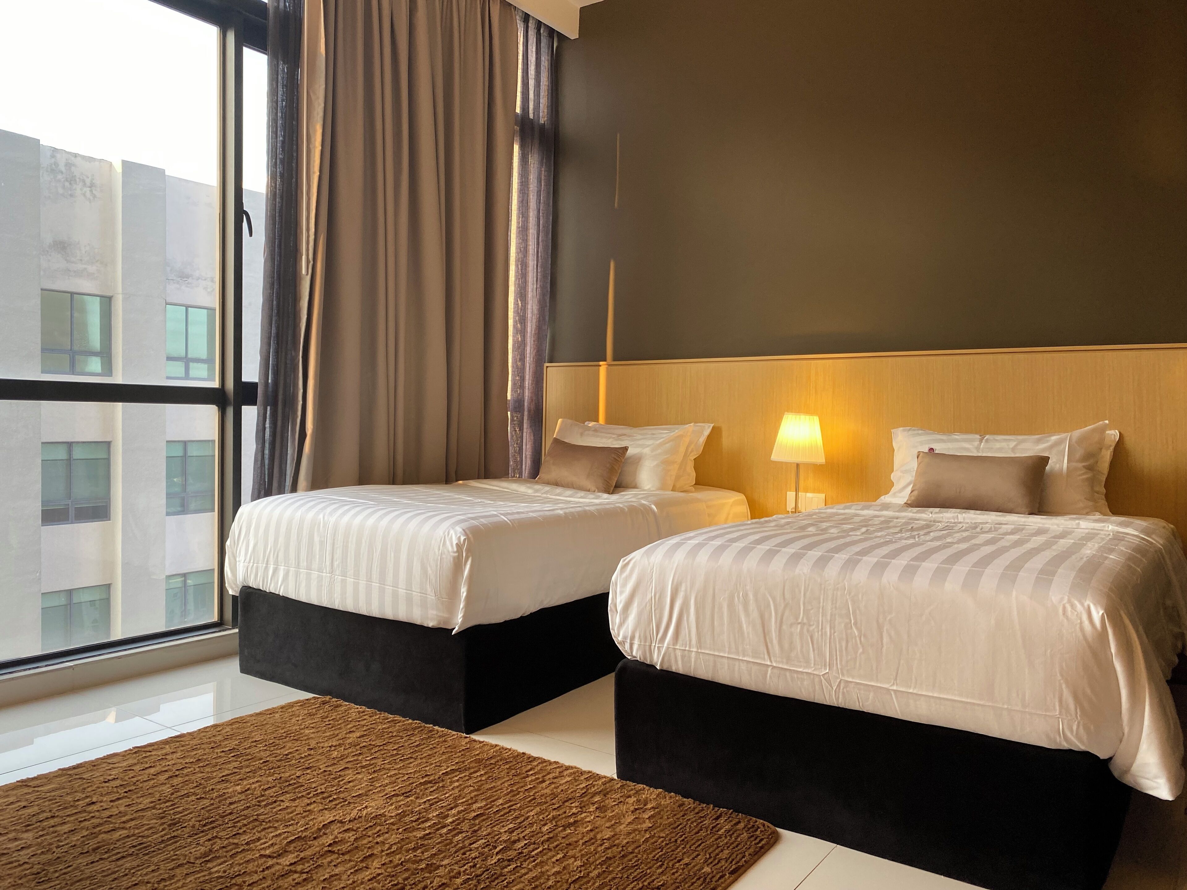 A hotel room with two beds, a large window, and a view of buildings outside.