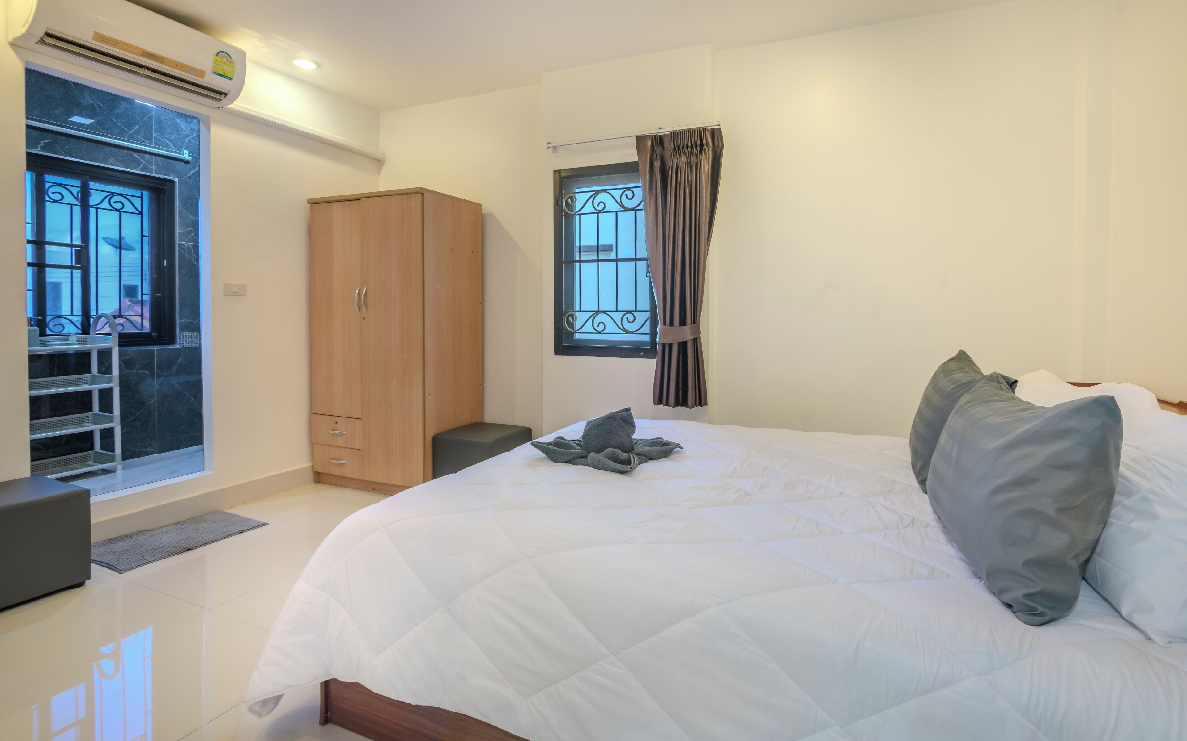 A bedroom with a bed, a wardrobe, a window with curtains, and an air conditioning unit.
