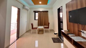 A modern living room with a flat-screen TV, a wooden cabinet, and a dining area with two chairs and a table. - Mantra Inn (Pune)