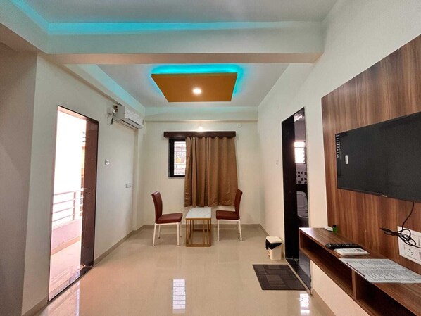 A modern living room with a flat-screen TV, a wooden cabinet, and a dining area with two chairs and a table. - Mantra Inn (Pune)