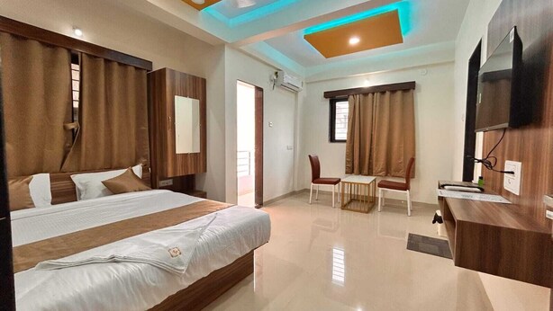 A hotel room with a large bed, a desk with a chair, a television, and a ceiling light fixture. - Mantra Inn (Pune)