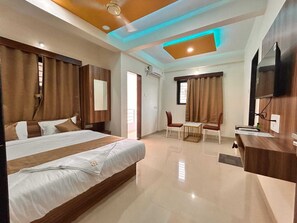 A hotel room with a large bed, a desk with a chair, a television, and a ceiling light fixture. - Mantra Inn (Pune)