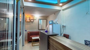 A modern reception area with a wooden reception desk, a ceiling fan, and a glass wall. - Mantra Inn (Pune)