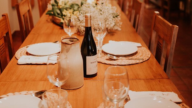 Une table de salle à manger en bois, mise avec des assiettes, des verres et une bouteille de vin, entourée de chaises.