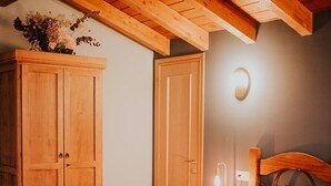Une chambre avec un plafond en bois, un lit avec une literie blanche, une table de chevet avec une lampe et une armoire en bois.