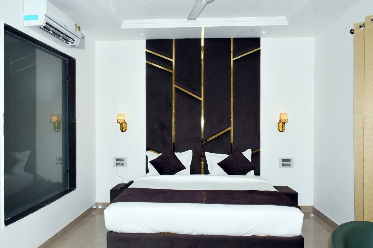 Una habitación de hotel moderna con una cama grande, una pared divisoria de vidrio, un aire acondicionado instalado en la pared y un aplique de techo.