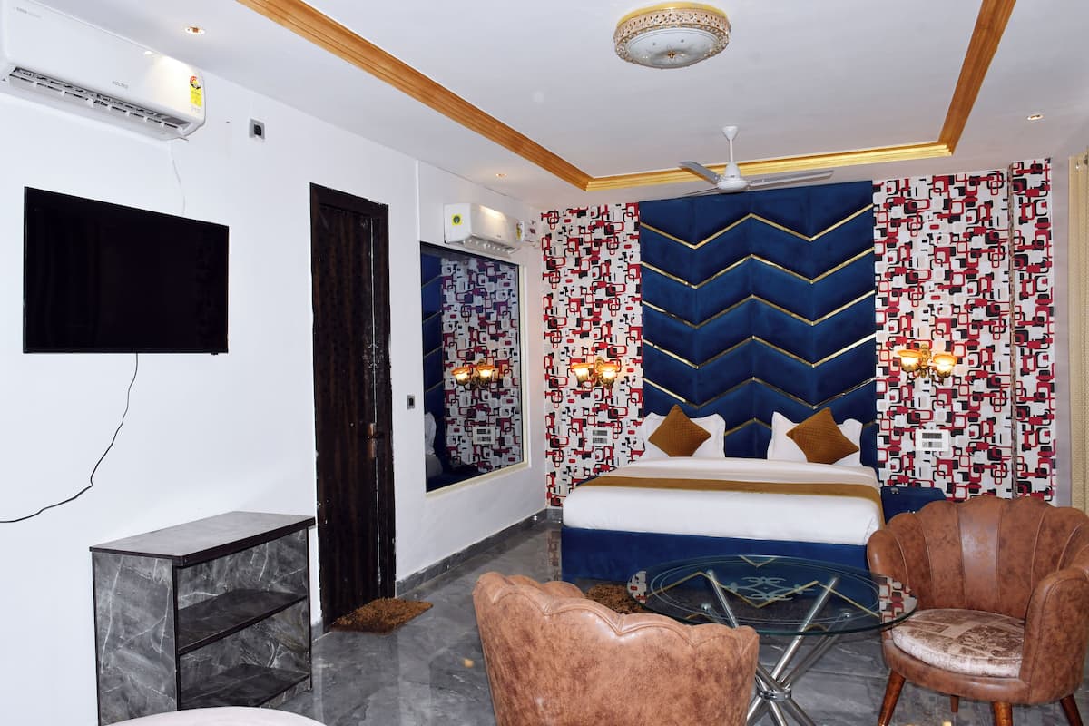 Una habitación de hotel moderna con cama, televisor, mesita de mármol y un área de descanso con dos sillones.