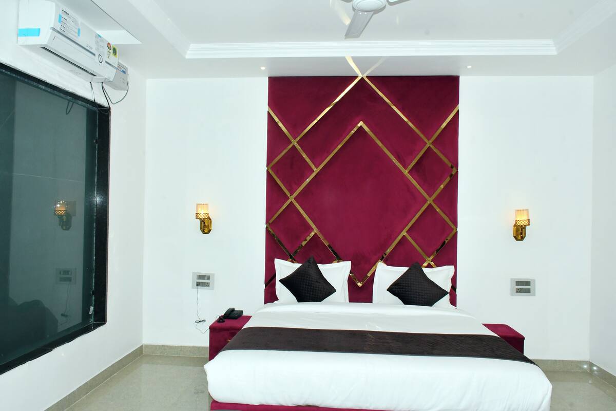 Habitación de hotel con una cama grande, cabecera roja, dos apliques de pared, ventilador de techo y una ventana con persianas.