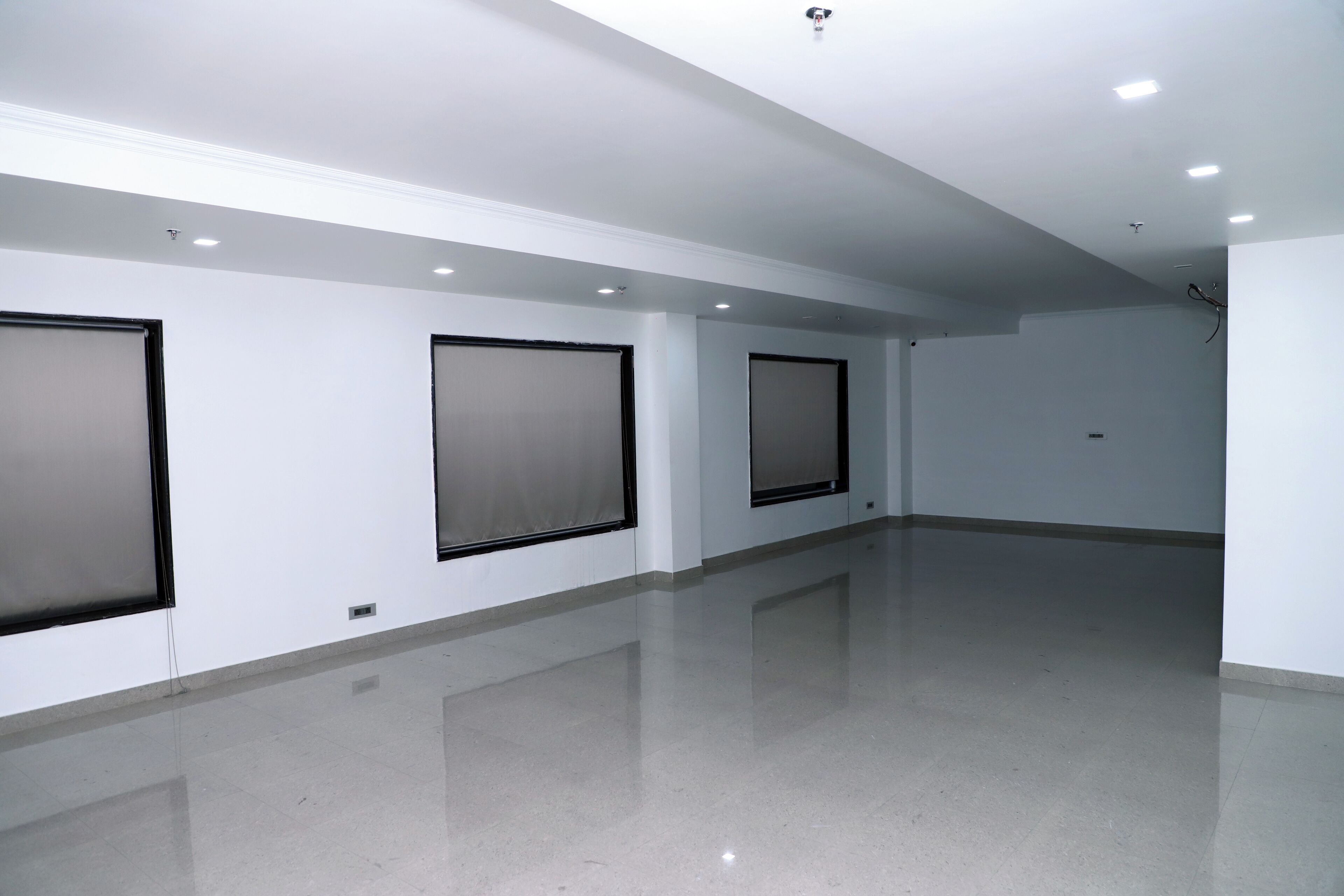 A spacious, empty room with white walls, large windows, and a shiny floor.