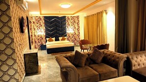 A hotel room with a large bed, a sofa, a small table, and a patterned wall. -  Bellazio Suites Hotel and Resort Bellazio (Bareilly)