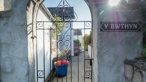 Un portail en fer forgé, sur lequel on peut lire l’inscription « Y BETHYN », mène à une cour intérieure agrémentée de plantes en pot.