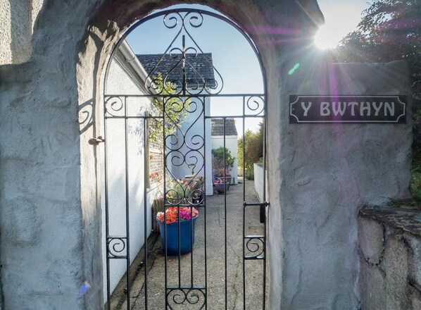 A wrought iron gate with a sign reading "Y BETHYN" leading to a courtyard with potted plants.
