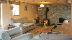 A cozy living room with a stone wall, a fireplace, and a television. - Y Cartws, Cardigan - Two Bedroom Cottage, Sleeps 4 (Cardigan)