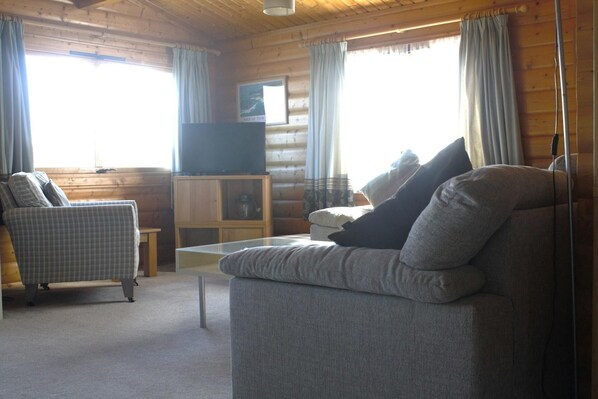 A cozy cabin interior with a sofa, a chair, a television, and a small cabinet. - Sea View Lodge, Porthgain (Llanrhian)