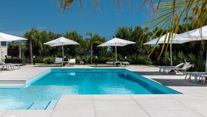 A rectangular swimming pool with white lounge chairs and umbrellas around it.