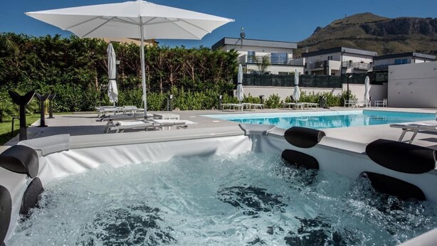 A hot tub area with a pool, umbrellas, and a modern building in the background.