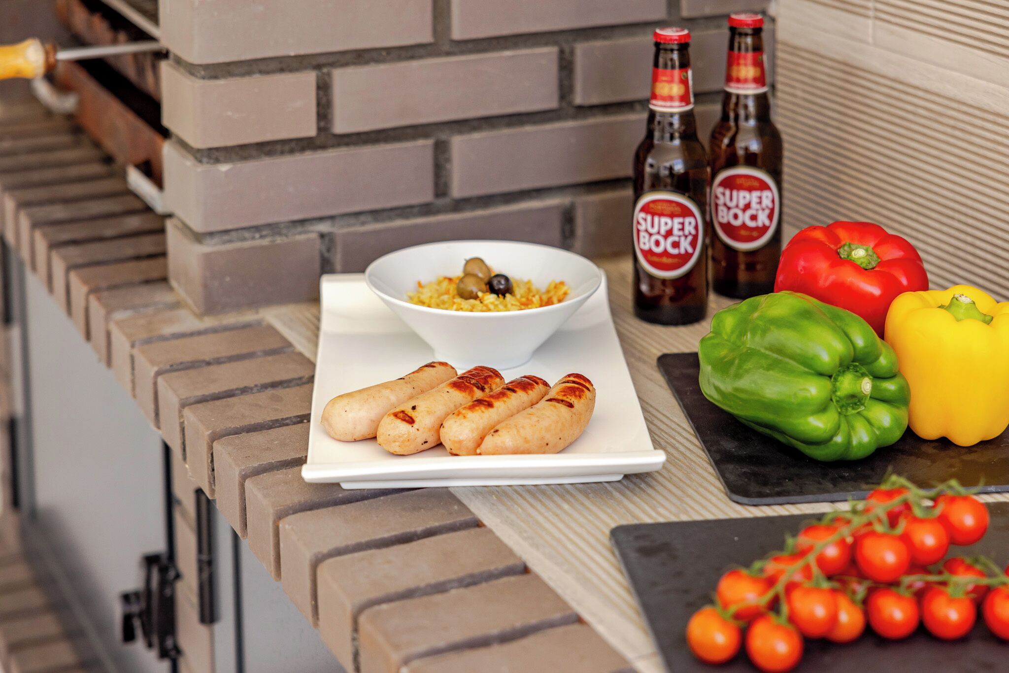 Een keukentafel met een witte schotel worstjes, een kom eten en een fles bier.