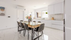 A modern kitchen with white cabinets, a stainless steel refrigerator, and a dining area with a glass table and grey chairs. - Villa Atlantica One luxury and unique with ocean view (Lourinha)