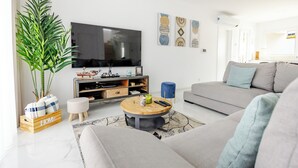 A modern living room with a grey sofa, a wooden coffee table, a TV, and a large plant. - Villa Atlantica One luxury and unique with ocean view (Lourinha)