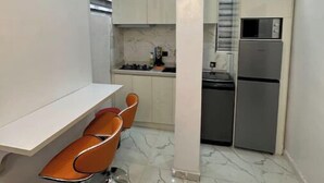 A compact kitchen with white cabinets, a built-in microwave, and a stainless steel refrigerator. There is a dining area with a white table and orange chairs. - Classic 2bedroom Flat in GRA

 (Ikeja)