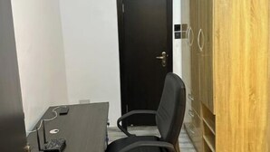 A small office space with a dark wooden desk, a black office chair, and a wooden wardrobe. - Classic 2bedroom Flat in GRA

 (Ikeja)