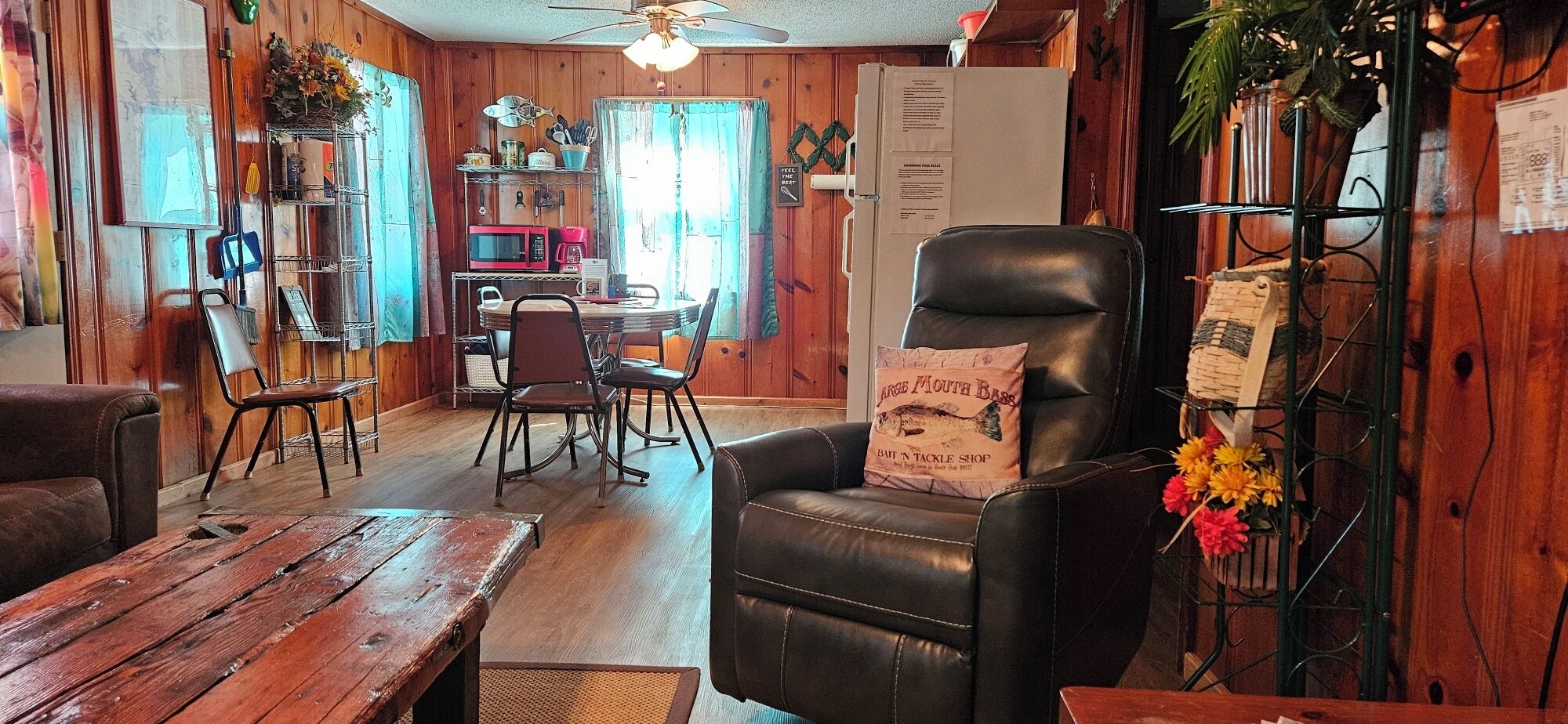 A cozy living room with a wooden interior, a dining area with chairs and a table, and a black leather chair with a pillow.