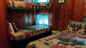 Une chambre avec un lit superposé, une courtepointe matelassée, des murs en bois et un tableau encadré accroché au mur.