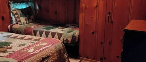 Ein schlicht eingerichtetes Schlafzimmer im Chalet-Stil mit zwei Etagenbetten, Holzwänden, einem Kleiderschrank und einem kleinen Tisch.