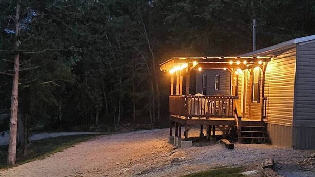 A cabin with a porch and string lights, surrounded by a gravel driveway and a grassy area. - Classy 3 Bed home w/ pool access - Moose Cabin (Elizabeth)