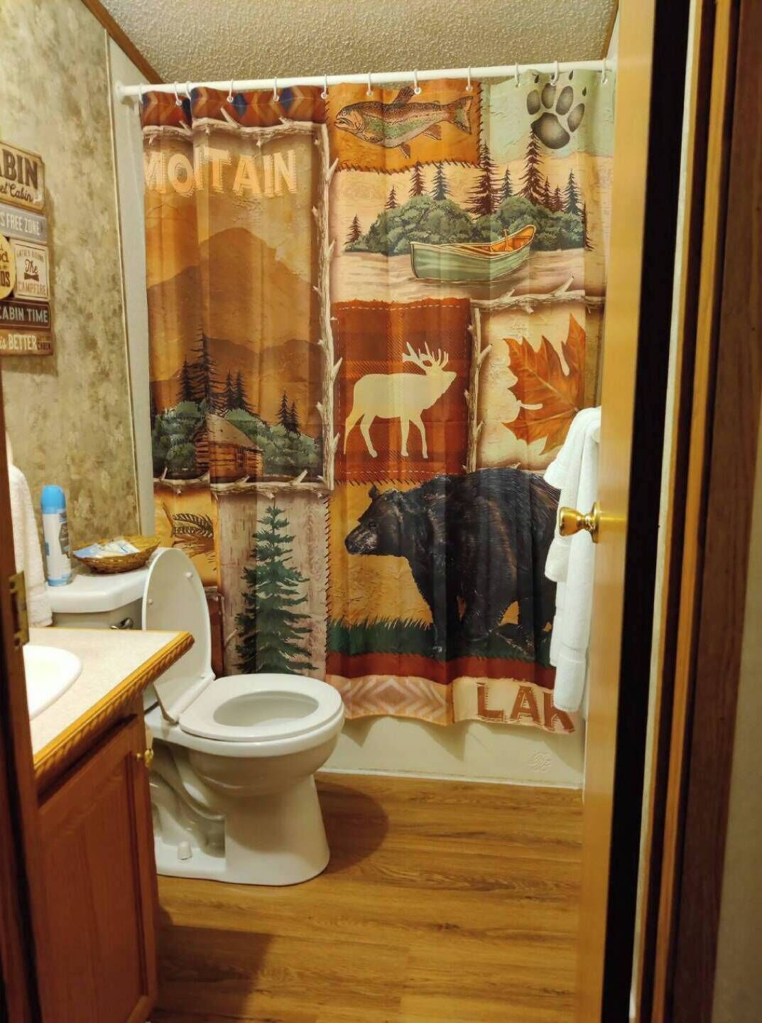 A bathroom with a shower curtain depicting a forest scene, a toilet, and a sink with a wooden countertop.