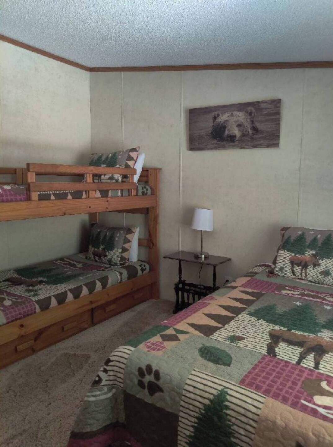 Una habitación con literas, una mesita con lámpara y un cuadro en la pared.