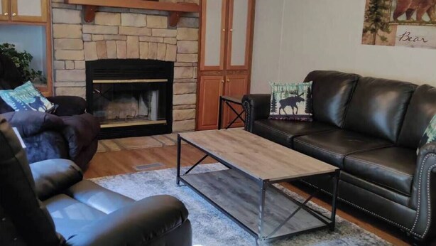 A living room with a fireplace, a ceiling fan, a black leather sofa, and a coffee table. - Entire Cabin on Norfork Lake with swimming pool (Elizabeth)