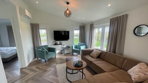 A spacious living area with a sofa, chairs, a coffee table, a TV, and a large window.