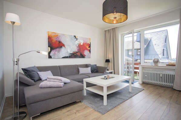 A modern living room with a grey sofa, white coffee table, and a large abstract painting on the wall.