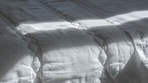 A bed with a white duvet in a room with a view through a window. - Amara Haven (Aigialeia)