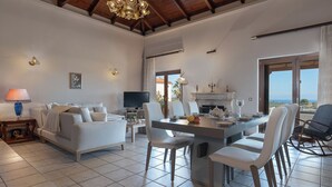 A spacious living area with a dining table, sofas, and a television. - Amara Haven (Aigialeia)
