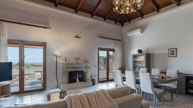 A spacious living area with a fireplace, dining table, and comfortable seating. - Amara Haven (Aigialeia)