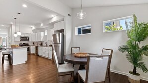 Een moderne keuken met witte kastjes, roestvrijstalen apparatuur en een eethoek met een houten tafel en stoelen.