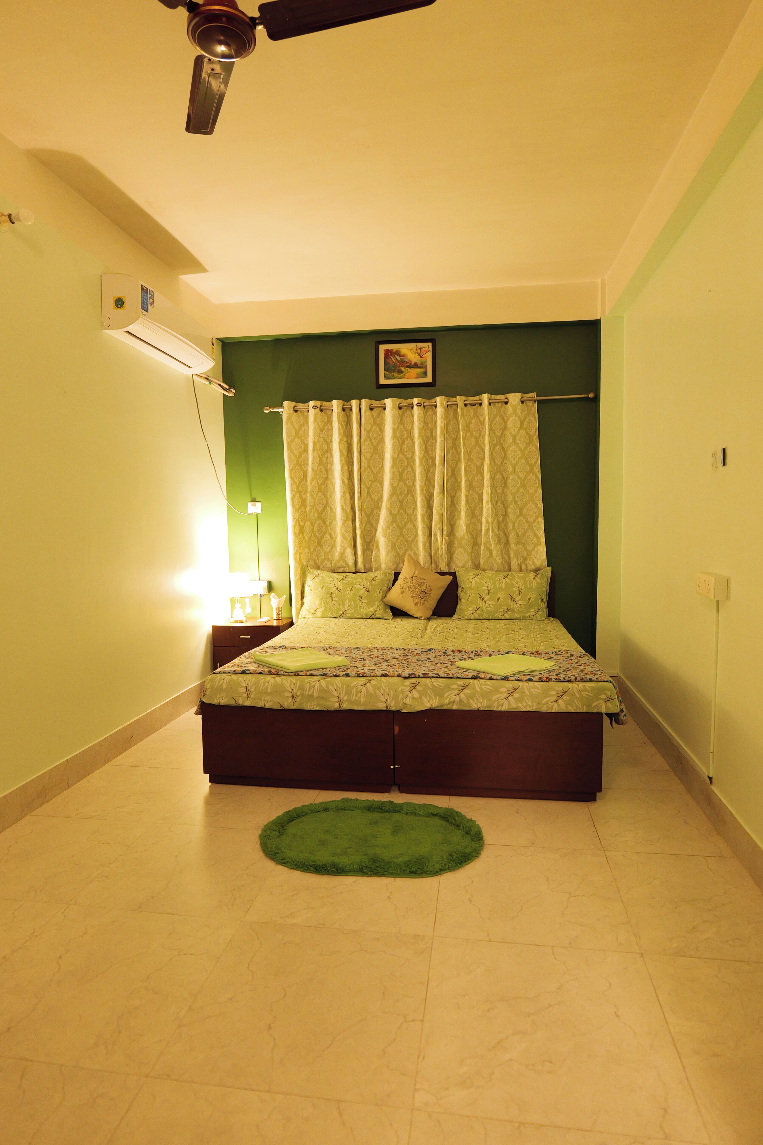 Ein Schlafzimmer mit einem Bett, einem Deckenventilator, einem grünen Teppich und einer Wand-Klimaanlage.