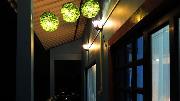 Un pasillo con techo de madera, luminarias esféricas verdes y amplios ventanales a un lado.